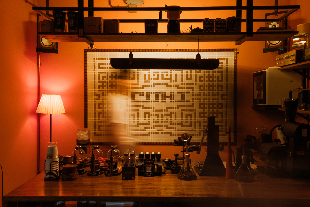 The brew bar under warm light, with the Cōhi mosaic sign on the wall